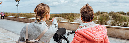 Zwei Frauen stehen mir ihren Fahrrädern an einer Promenade. Eine von ihnen zeigt in Richtung Horizont.  - zum Artikel 'Gutes September-Ergebnis lässt auf zufriedenstellendes Tourismusjahr 2023 hoffen '