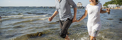 Ein Paar läuft lachend durch das seichte Wasser am Strand bei Glücksburg. - zum Artikel 'Deutsche Post Glücksatlas 2020: Schleswig-Holstein und Hamburg auf Platz 1'