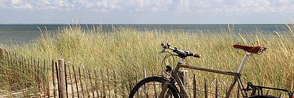 Ein Fahrrad lehnt an den Dünen am Strand auf Sylt.  - zum Artikel 'Bilanz Schleswig-Holstein-Tourismus 2022: Bestes Übernachtungsjahr, auch Gästezahl fast auf 2019 Niveau, Aufgaben zur Zukunftssicherung des Tourismus bleiben'