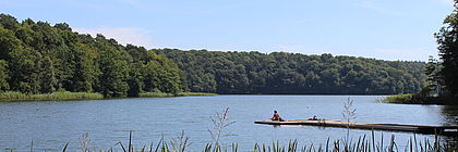 Ein Bild vom Lütauer See. Eine Frau liegt auf dem Badesteg am See.  - zum Artikel 'Buchungslage im Schleswig-Holstein-Tourismus für Pfingsten und Ausblick auf den Sommer 2023'