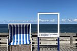 Ein Selfie-Rahmen steht als Fotomotiv neben einem blauweißen Strandkorb vor der Nordsee auf Sylt.