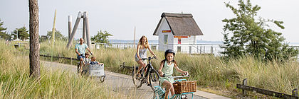 Eine Familie genießt einen sommerlichen Ausflug per Rad in Scharbeutz. - zum Artikel 'Mit dem Rad entlang der Küste in Schleswig-Holstein'