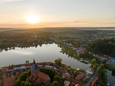 Luftaufnahme von Mölln bei Sonnenuntergang mit Altstadt, Kirche, See, umliegenden Häusern und grüner Landschaft.