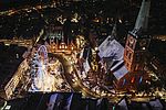 En udsigt fra oven over det maritime julemarked på Koberg i Lübeck. Det er mørkt, julemarkedet og Jakobskirken er oplyst. Der ligger lidt sne på tagene. 